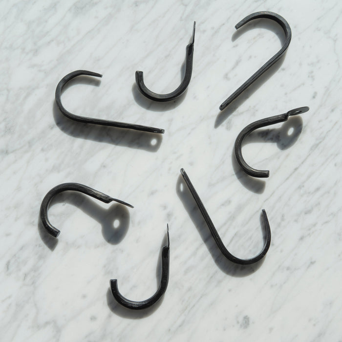 A collection of iron wall hooks with an uncoated matte finish, displayed on a marble surface.